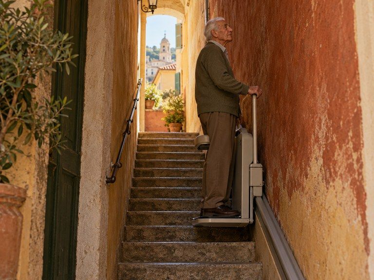 Un homme âgé debout sur un monte-escalier à station debout, dans l’escalier étroit d’une maison de vieille ville